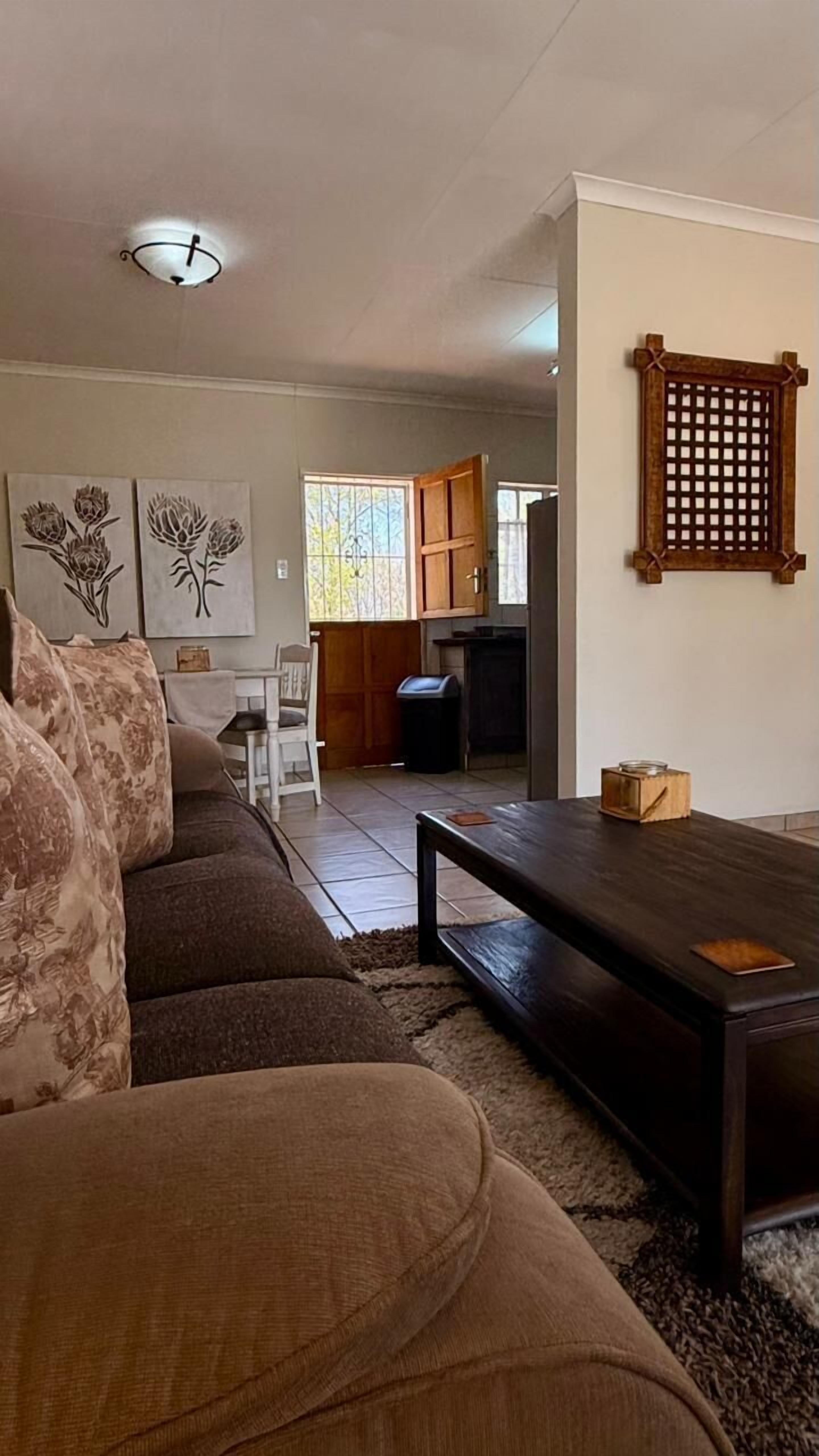A living room with a dark wooden coffee table, a sofa with floral cushions, and a dining area with a white table and chairs.