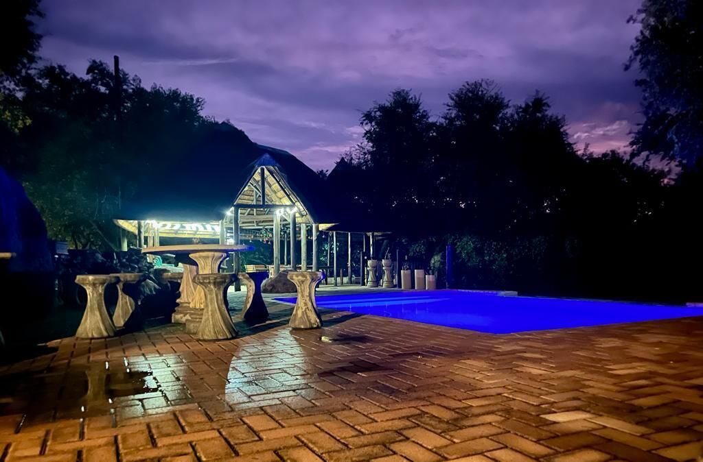 A well-lit outdoor area with a swimming pool, stone tables, and a building with a glass roof.