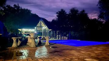A well-lit outdoor area with a swimming pool, stone tables, and a building with a glass roof.