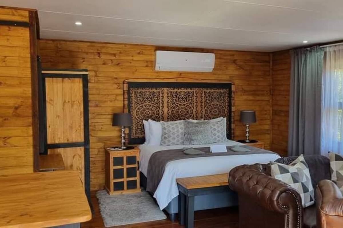 A wooden-paneled room with a bed, a small table, a chair, and a sofa.