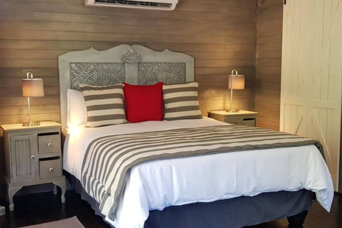 A bedroom with a wooden headboard, a bed with striped bedding, two bedside lamps, and a nightstand with drawers.