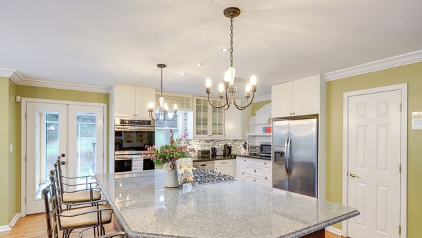 A kitchen with a large island, stainless steel appliances, and a chandelier.