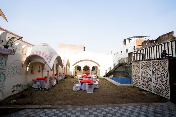 An outdoor courtyard with a dining setup, including round tables and chairs, and a staircase leading to a building. - Hotel RR 62 - Jaipur City Centre Hotel (Jaipur)