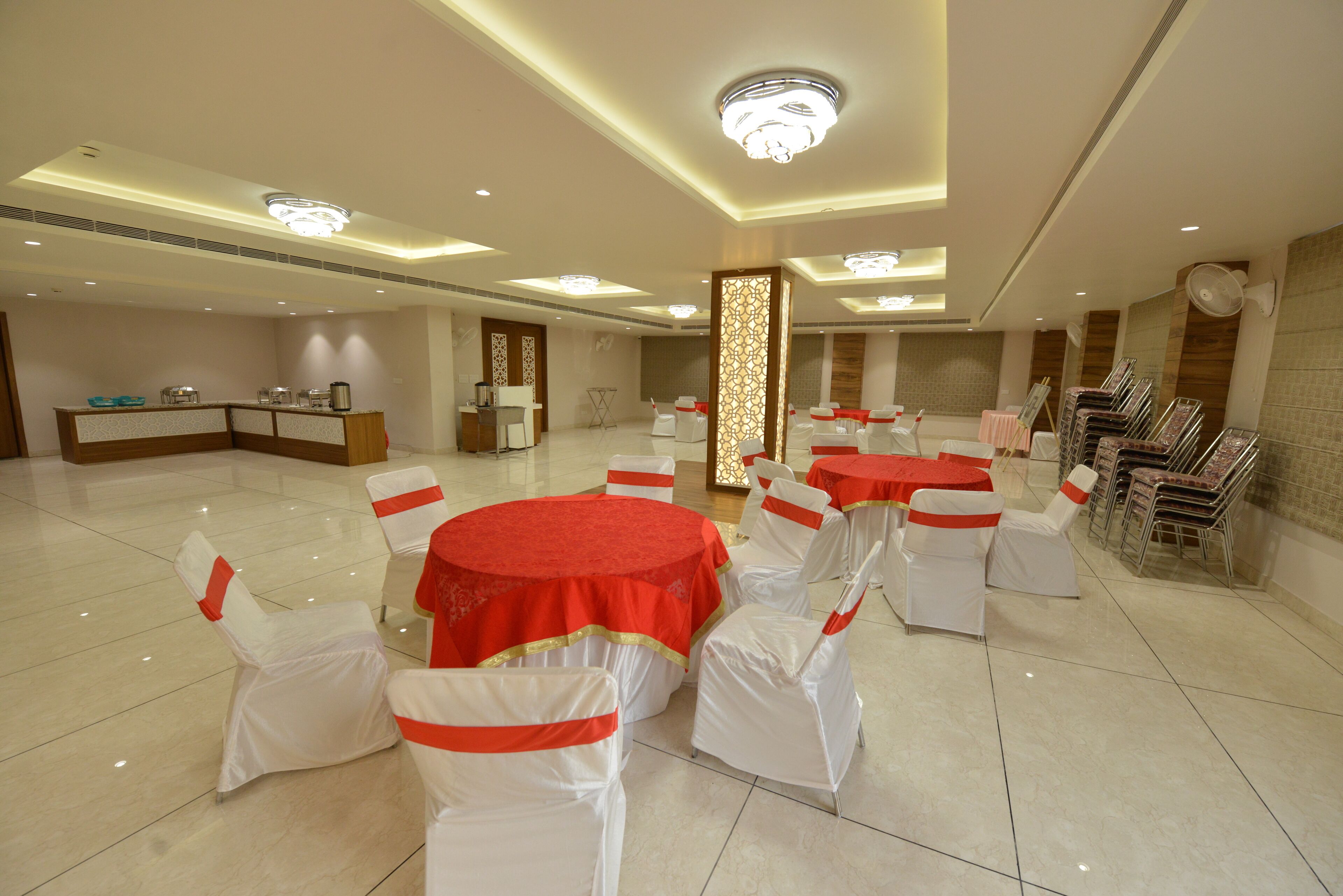 A spacious banquet hall with round tables covered in red tablecloths and white chairs with red sashes.