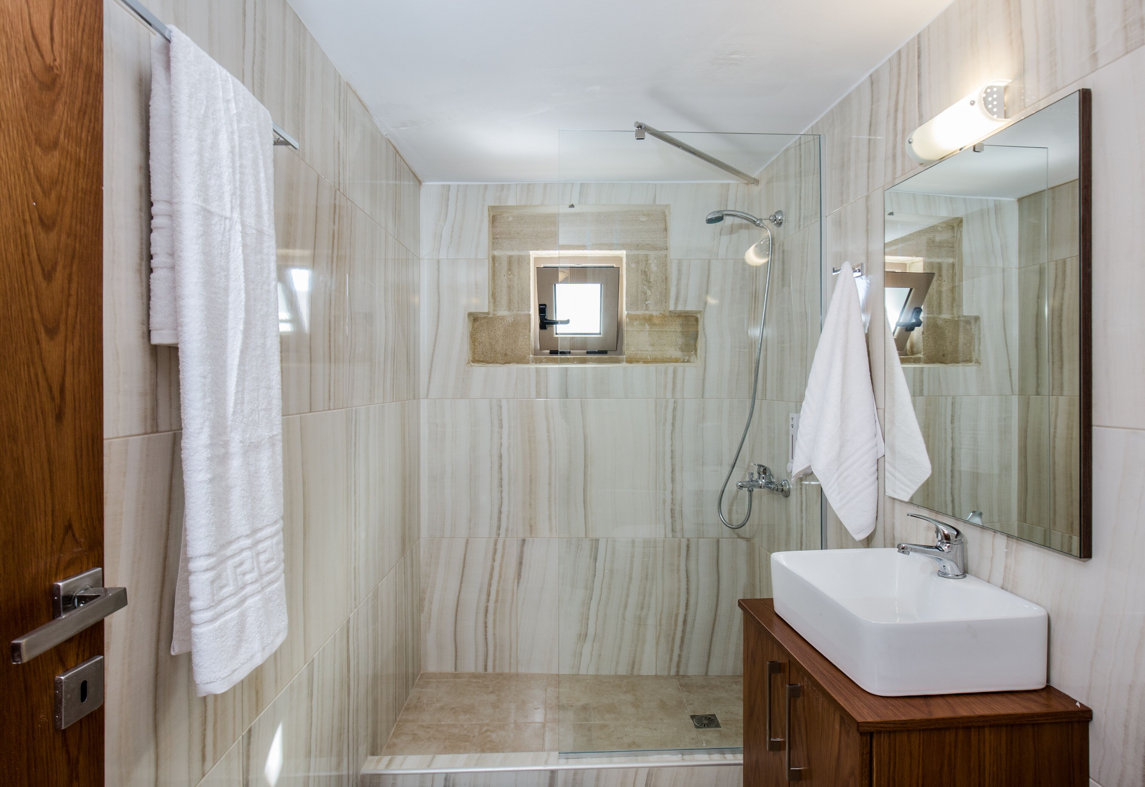 A modern bathroom with a glass-enclosed shower, a wooden vanity with a white sink, and a large mirror.