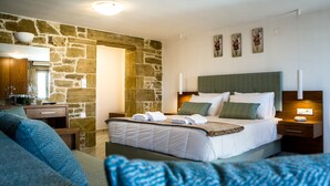 A bedroom with a stone wall, a bed with white linens, a wooden nightstand, and a blue sofa. - Agarathos Homes (Kissamos)