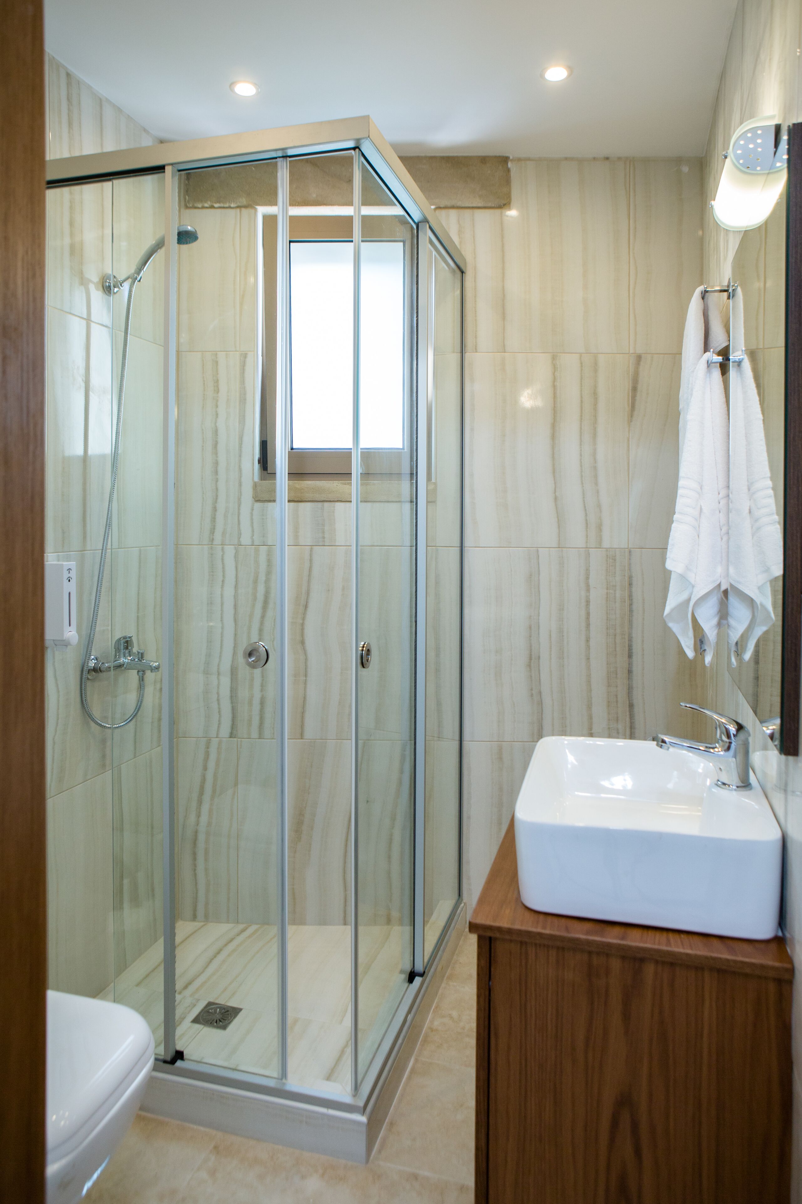 A modern bathroom with a glass-enclosed shower, a white sink, and a wooden cabinet.