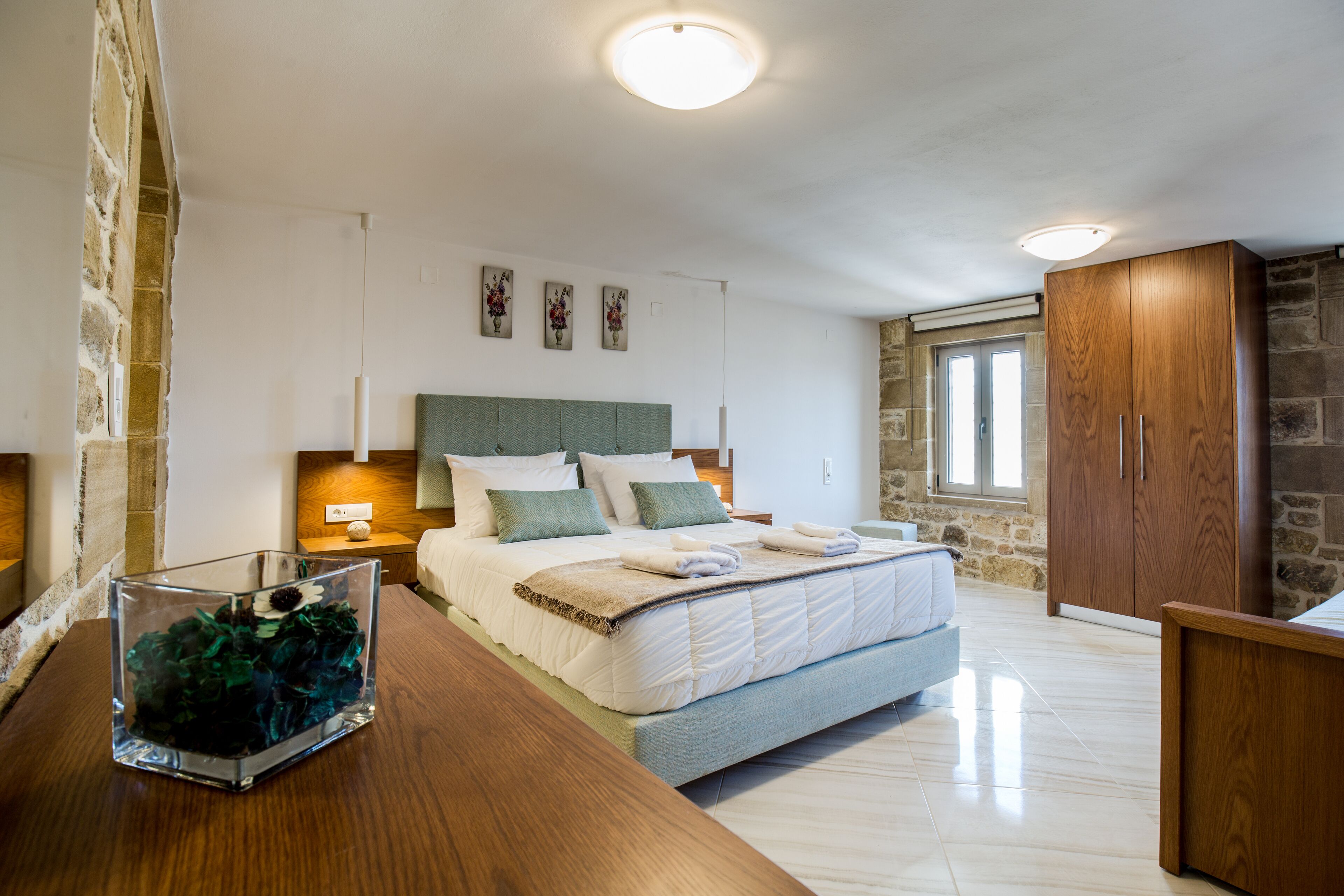 A modern bedroom with a large bed, a wooden dresser, and a stone wall.