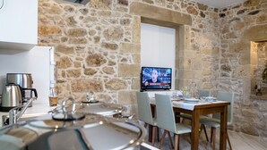 A stone-walled room with a television, a table set for dining, and a kettle on the counter. - Agarathos Homes (Kissamos)