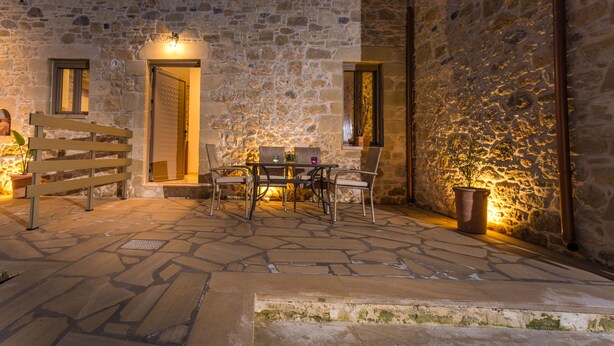 A stone courtyard with a table and chairs, a wooden bench, and a potted plant. - Agarathos Homes (Kissamos)