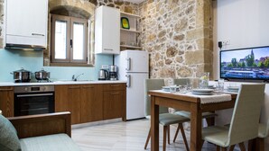A modern kitchen with stone walls, wooden cabinets, and a dining area with a table and chairs. - Agarathos Homes (Kissamos)