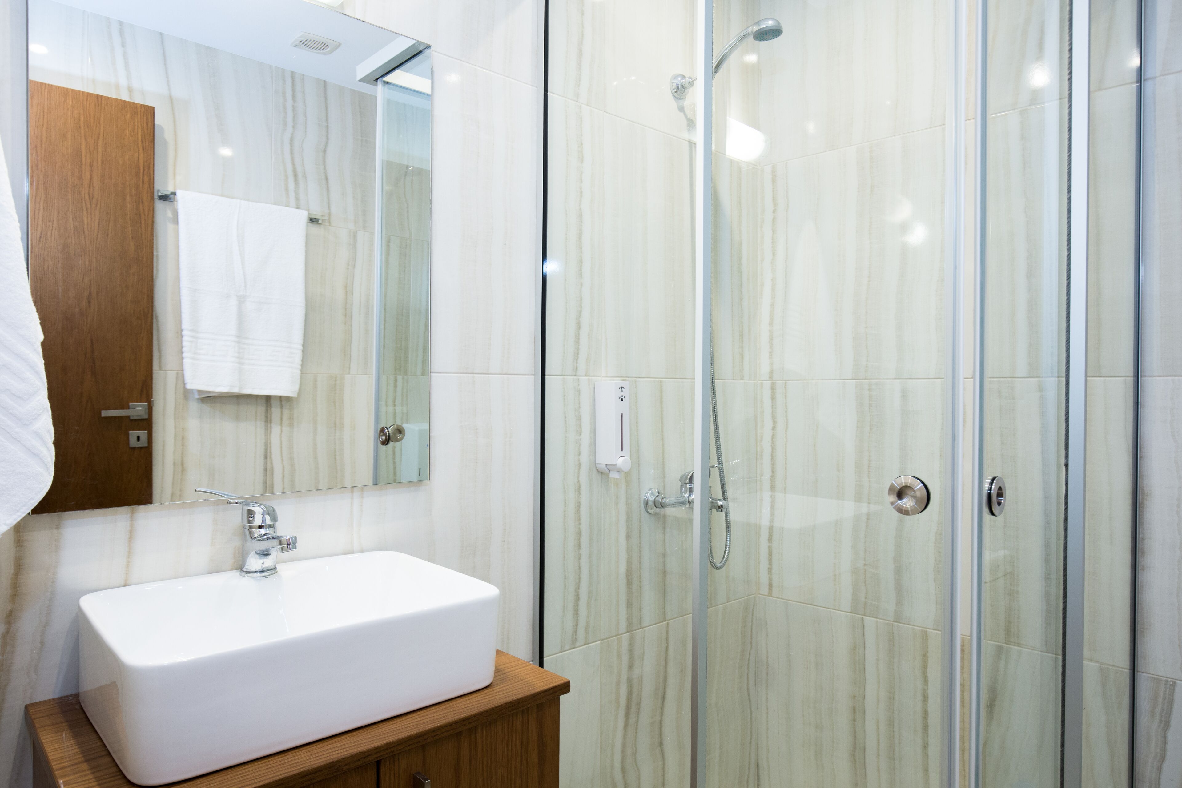 A modern bathroom with a white sink, a glass shower enclosure, and a wooden vanity.