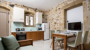 A compact kitchen with stone walls, wooden cabinets, and a dining area with a table and chairs. - Agarathos Homes (Kissamos)