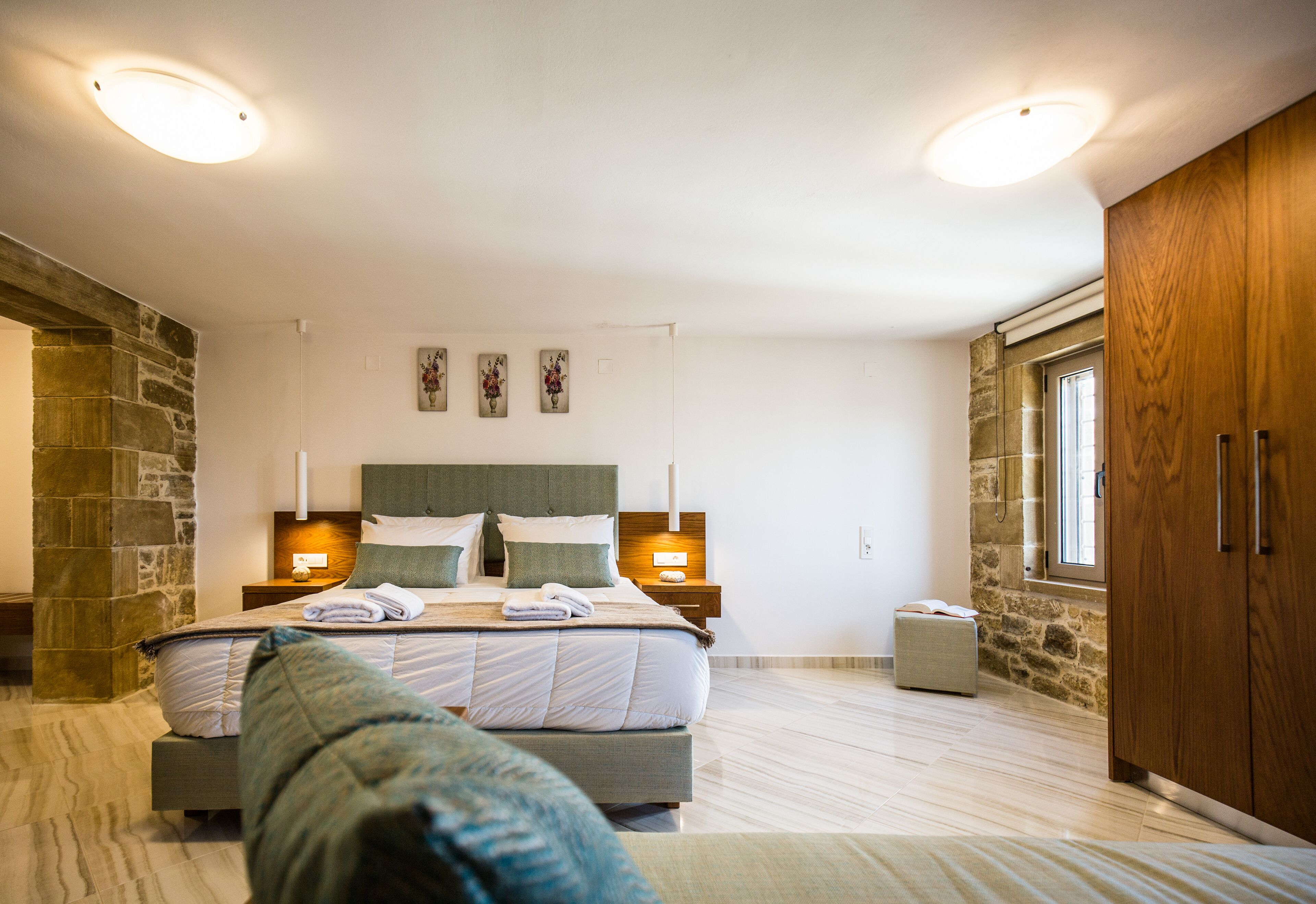 Un dormitorio moderno con una cama grande, paredes de piedra, armario de madera y dos lámparas de noche.