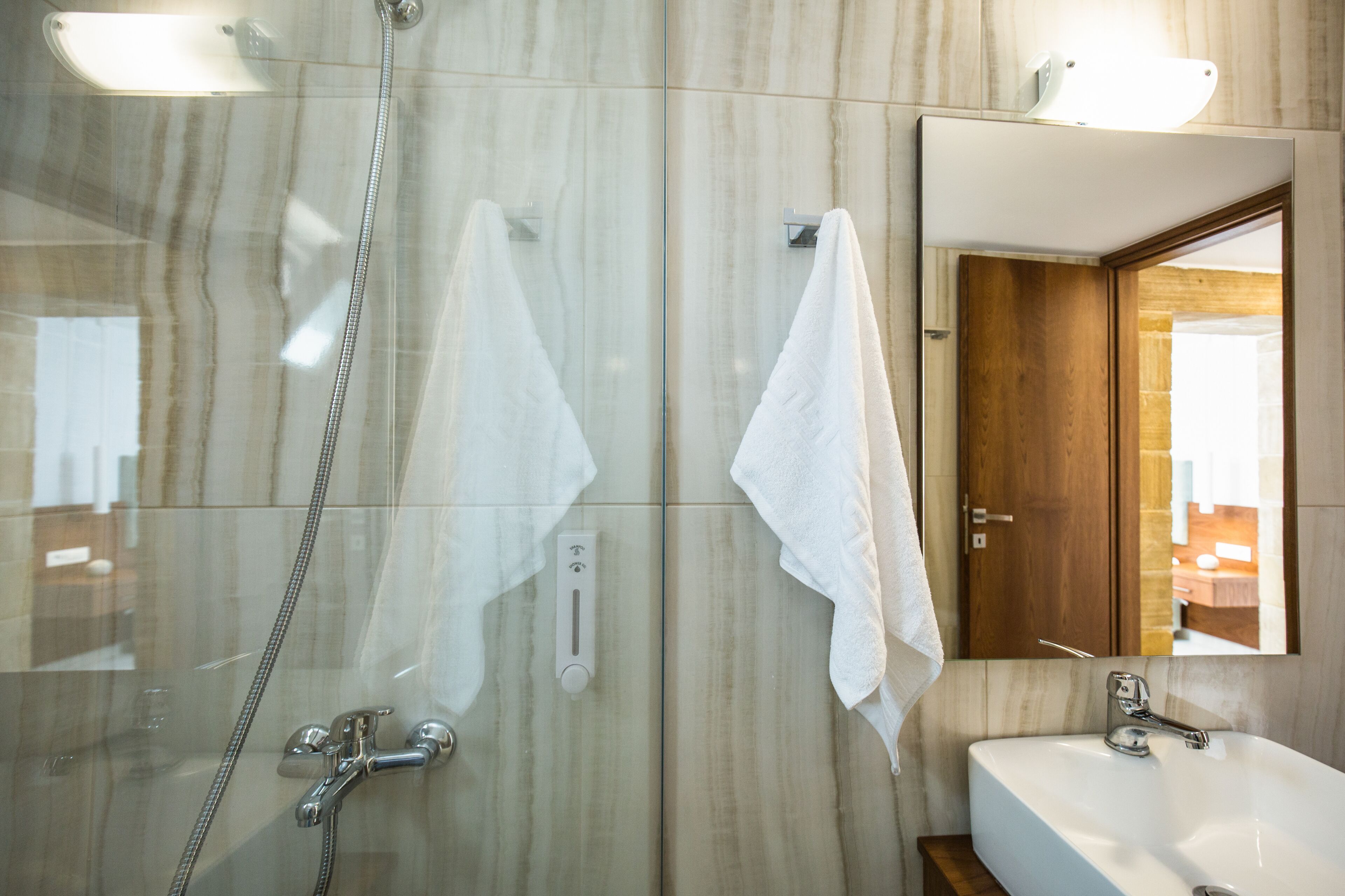 Un baño moderno con ducha envuelta en vidrio, un lavabo blanco y una puerta de madera.