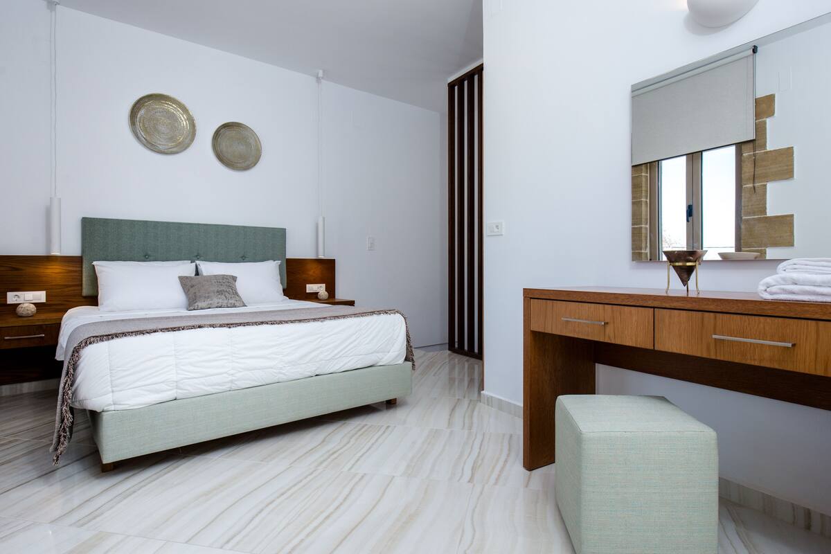 A modern bedroom with a bed, bedside tables, a dresser, and a mirror.