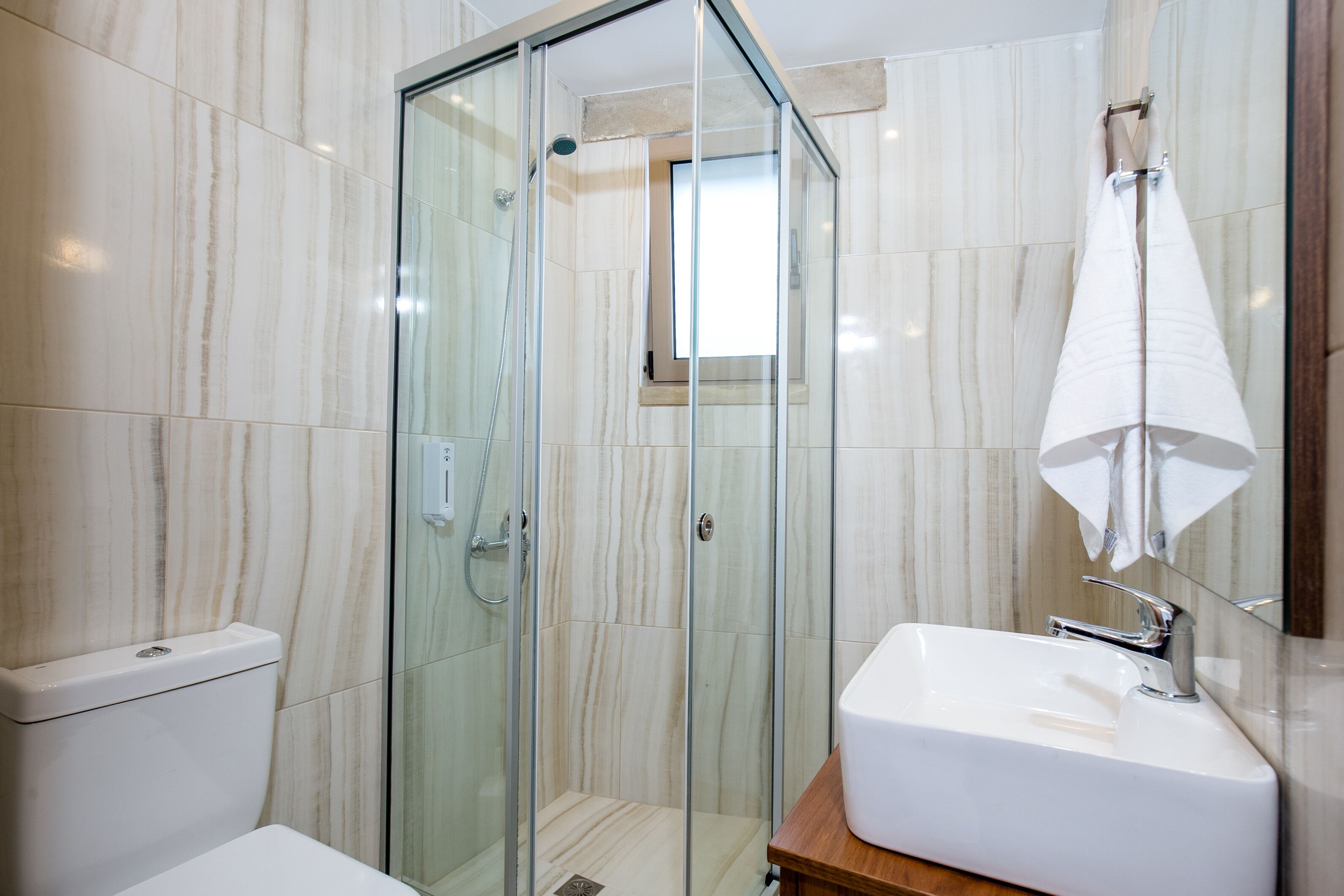A modern bathroom with a glass-enclosed shower, a white sink, and a toilet.
