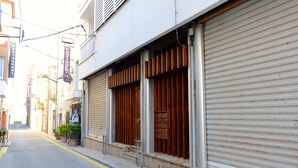 A narrow street with closed shuttered shops and a restaurant sign. - PUIG SUREDA 13-2B (L'Escala)