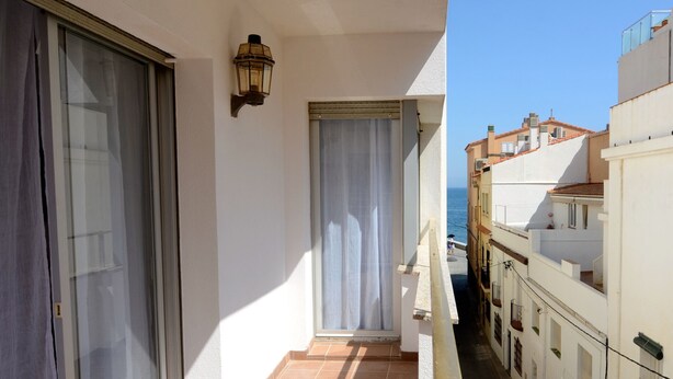 A narrow balcony with a view of the sea, a door with a curtain, and a wall-mounted light fixture. - PUIG SUREDA 13-2B (L'Escala)
