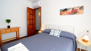 A bedroom with a bed, a wooden desk, a potted plant, a door, and a wall-mounted air conditioner. - PUIG SUREDA 13-2B (L'Escala)