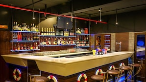 Zona de bar con múltiples estantes llenos de botellas de licor, una barra y taburetes.