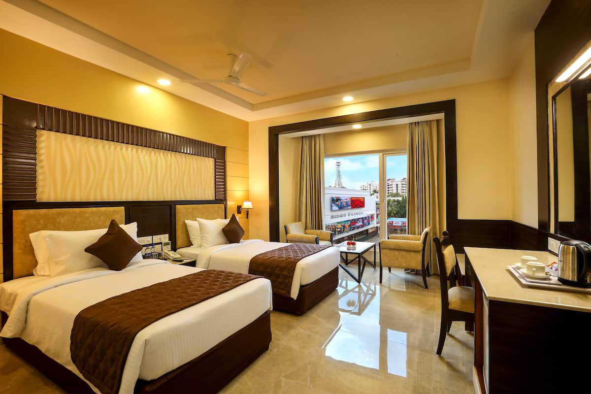A hotel room with two beds, a desk, a chair, and a view of the city.