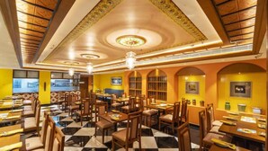 Un restaurante con suelo a cuadros, techo de madera y paredes amarillas. Mesas y sillas dispuestas para comer.