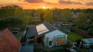A residential area with houses, a prominent house with a sloped roof and solar panels, surrounded by trees and greenery. - Spacious house & spa near forest, beach and sea and the cozy village of Bergen (Bergen)