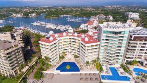 A hotel with a central courtyard pool, multiple balconies, and a marina in the background.