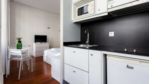 Een moderne keuken met witte kasten, een zwart aanrecht en een magnetron. Er is een gootsteen met een kraan, een kleine groene plant op een witte tafel, en een televisie op de achtergrond.