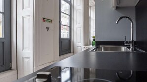 Een moderne keuken met een zwart aanrecht, een roestvrijstalen spoelbak en een raam met uitzicht op gebouwen.