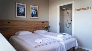 A hotel room with two beds, a wooden headboard, a shower area, and two framed pictures on the wall.
