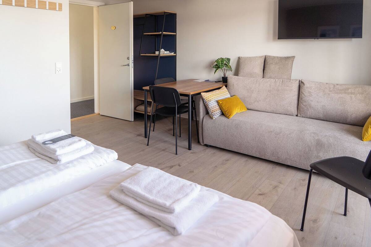 A hotel room with two beds, a sofa, a desk, and a TV.