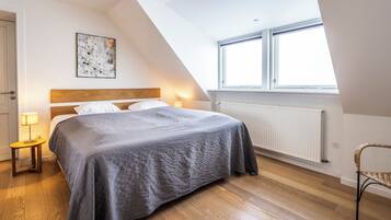 A bedroom with a bed, a nightstand, a chair, a window, and a radiator.