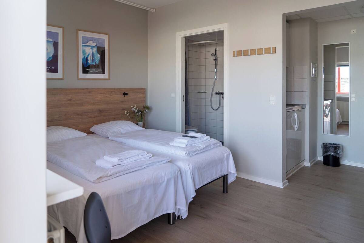 A hotel room with two beds, a wooden headboard, a shower, and a small bathroom.