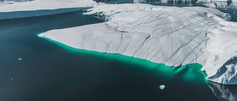 An aerial view of a large iceberg with a clear turquoise water channel.