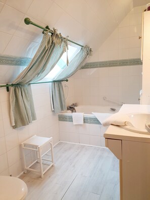 Ein Badezimmer mit Badewanne, Toilette, einem kleinen weißen Hocker und einer Duschvorhang mit gestreiften Handtüchern.