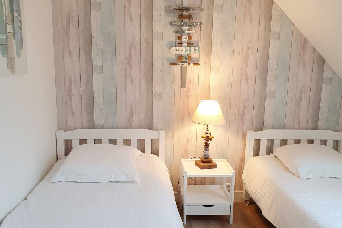 Een slaapkamer met twee bedden, een wand van houten latten, een nachtkastje met een lamp en een bordje aan de muur.