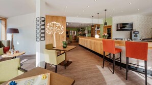 Un hall d’hôtel moderne avec un comptoir d’accueil en bois, un espace salon et un téléviseur fixé au mur.