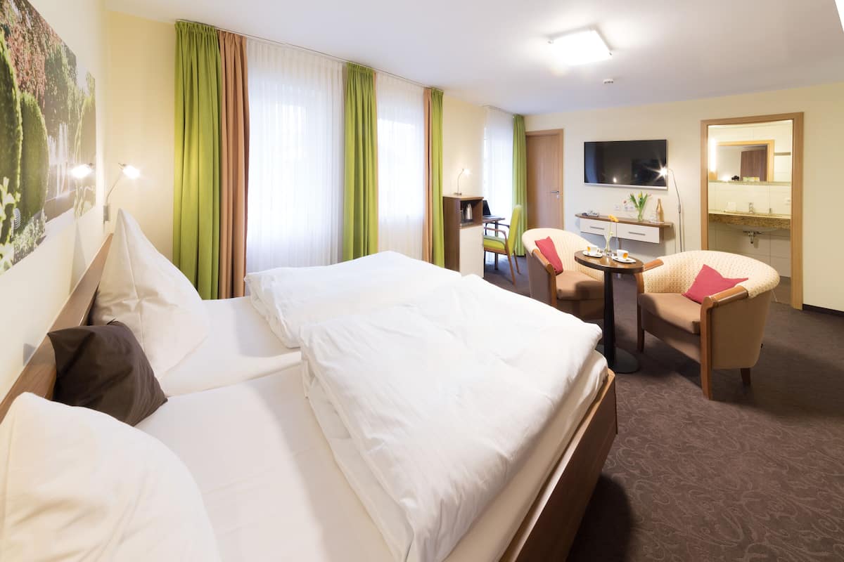 A hotel room with a large bed, a desk with a chair, a TV, and a bathroom with a mirror.