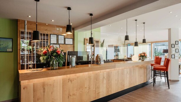 Un espace d’accueil doté d’un comptoir en bois, de luminaires suspendus noirs et d’une vitrine en verre où sont exposées des fleurs.