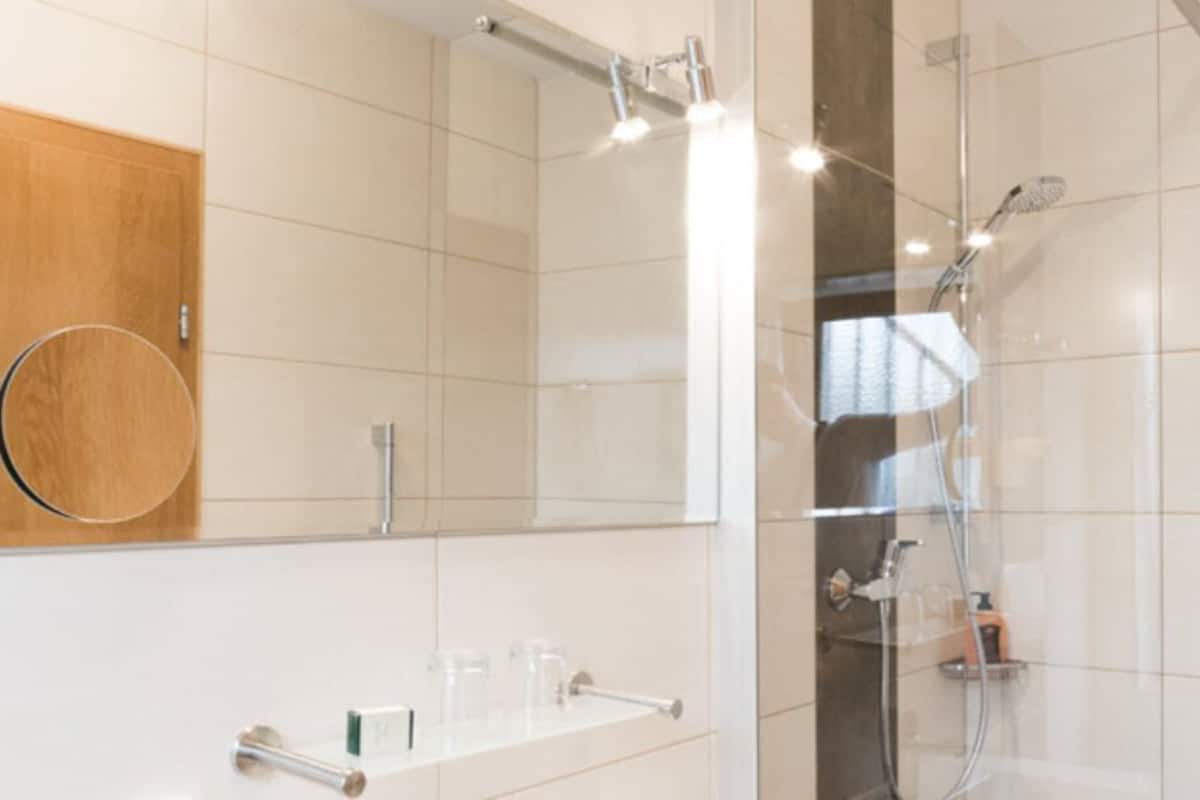 Un baño moderno con cabina de ducha de vidrio, un mueble de tocador de madera y un lavabo blanco con espejo.