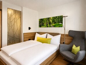 A modern hotel room with a bed, a chair, a painting, and a wall-mounted lamp. - Vitalhotel Garni Vier Jahreszeiten (Bad Fuessing)