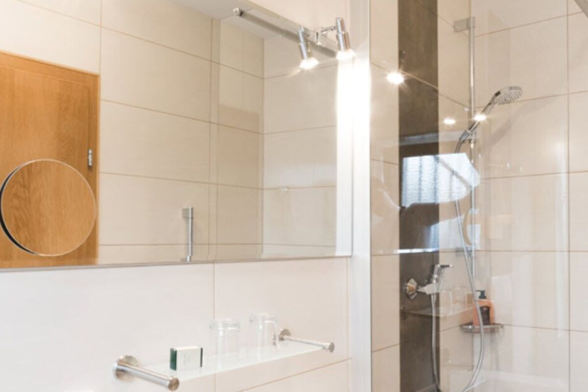 Un baño moderno con cabina de ducha de vidrio, un mueble de tocador de madera y un lavabo blanco con espejo.