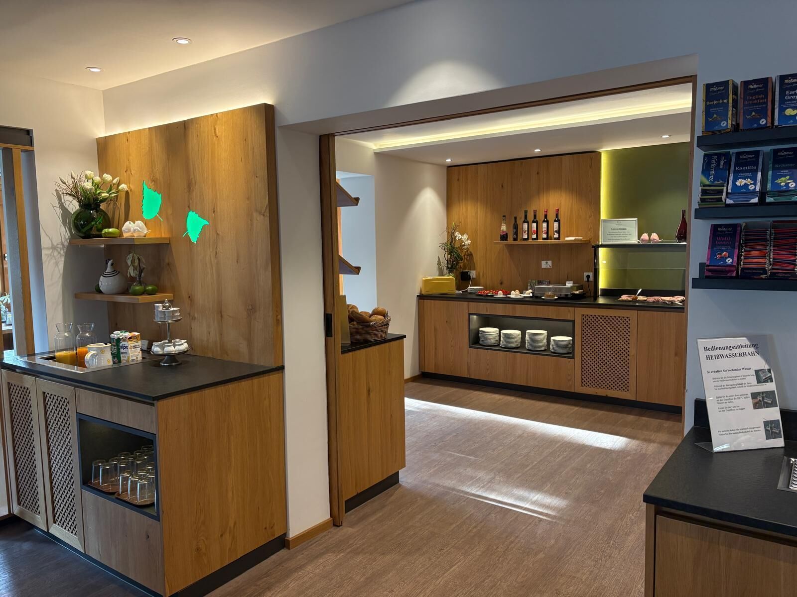 A modern hotel reception area with wooden paneling, a counter with amenities, and a visible kitchen area.