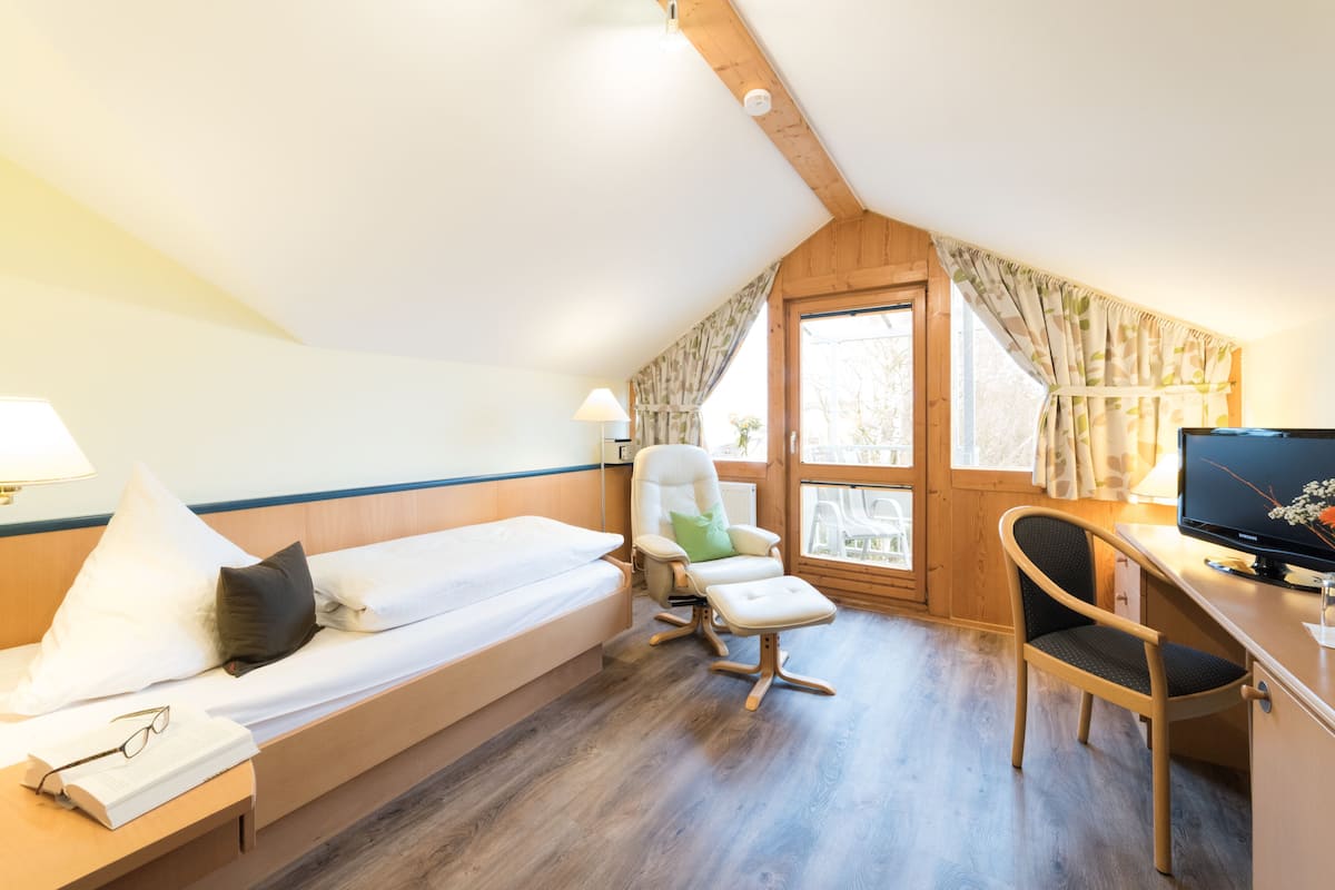 A room with a bed, a desk, a chair, and a window with curtains.