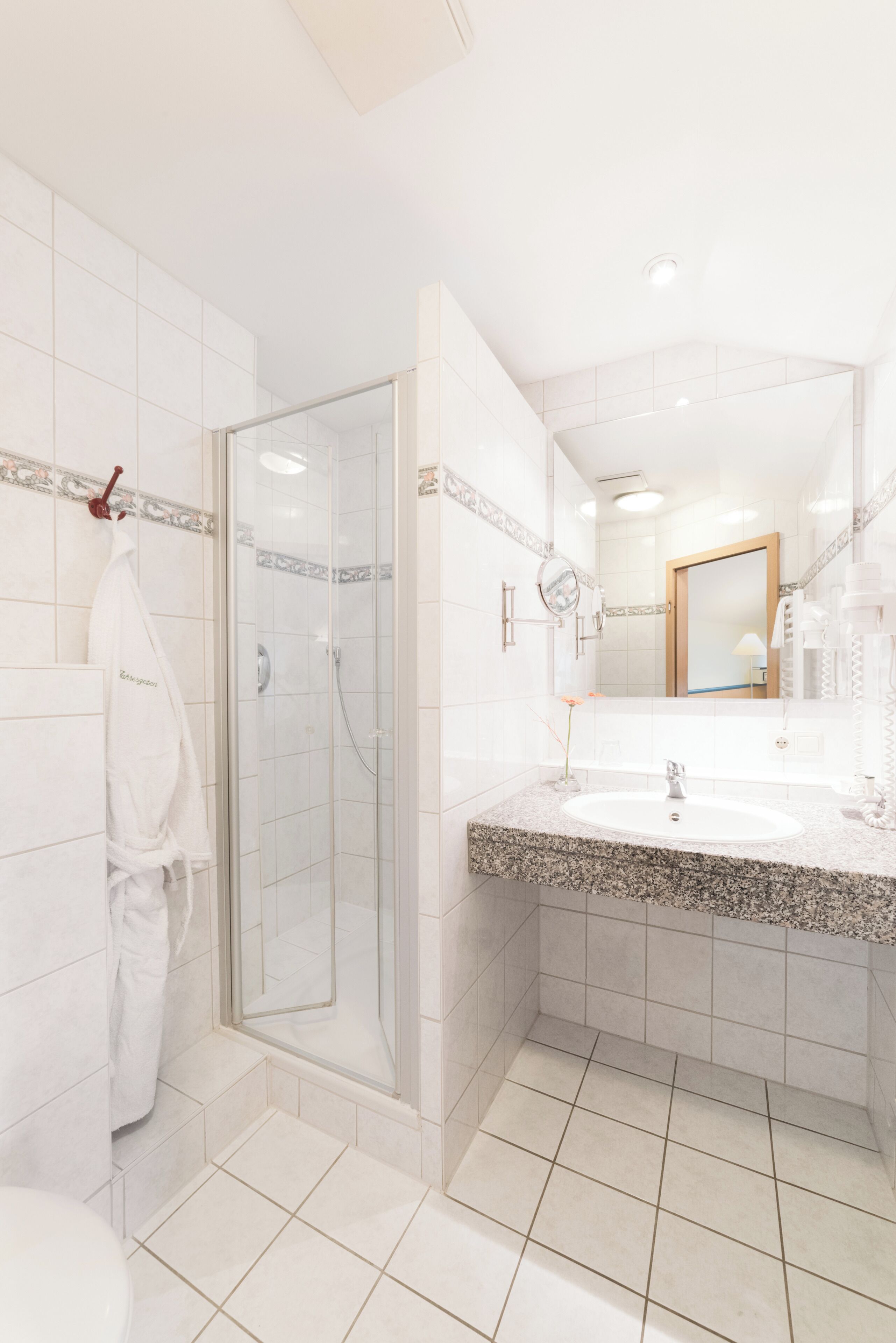 A modern bathroom with a glass-enclosed shower, a sink with a marble countertop, and a large mirror.