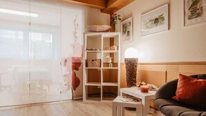 Un salon comprenant un canapé, une table d’appoint, une lampe, une bibliothèque et une porte vitrée donnant sur un coin repas.