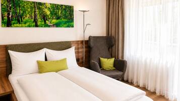 A hotel room with a bed, a chair, a painting of a forest, and sheer curtains.
