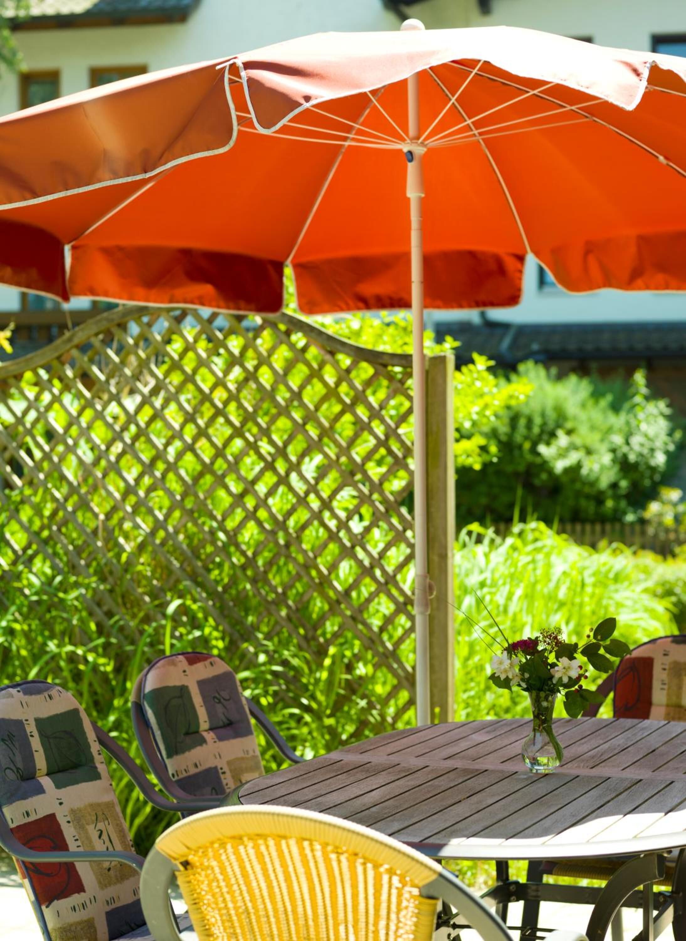 An outdoor patio with a wooden table, a yellow chair, and a red umbrella.